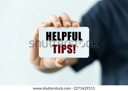 Helpful tips text on blank business card being held by a woman's hand with blurred background. Business concept about useful tips and tricks.