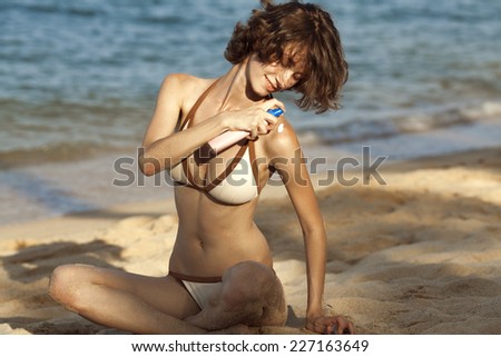 Young woman applying protective lotion before sunbathing at beach