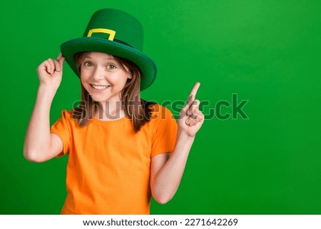 Photo of small charming girl touch headwear indicate finger empty space isolated on green color background