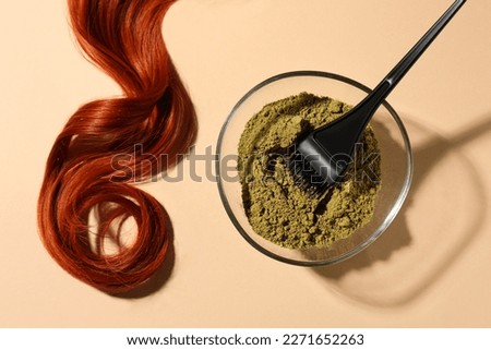 Bowl of henna powder, brush and red strand on beige background, flat lay. Natural hair coloring
