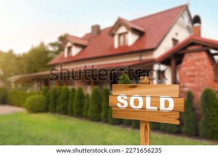 Wooden Sold sign near new house outdoors. Space for text