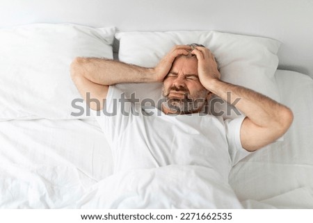Unhappy sick middle aged man lying in bed with closed eyes at home, touching head, tired male wake up with headache in the morning, suffering from chronic migraine, view above, copy space Royalty-Free Stock Photo #2271662535