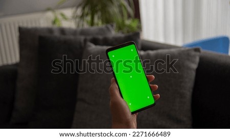 Back view of young europen woman who is using chroma key smartphone screen.She is sitting on the sofa in her cozy living room.