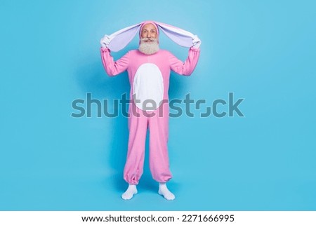 Full length photo of positive funny cheerful senior man dressed pink rabbit costume arms hold long ears isolated on blue color background