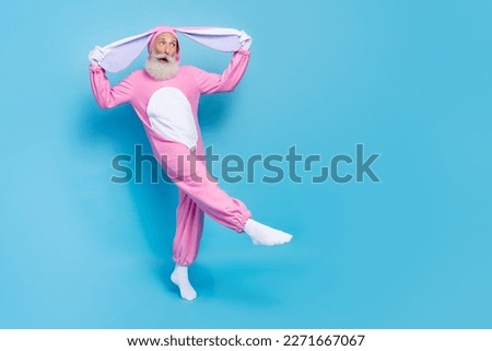 Full size photo of cheerful elderly pensioner wear pink bunny costume arms hold ears look empty space isolated on blue color background