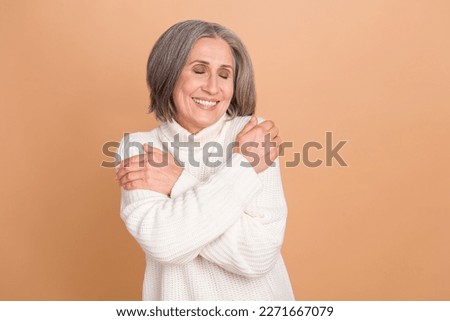 Photo portrait of nice satisfied pensioner lady gray hair cuddles herself new warm white turtleneck clothes isolated on beige color background