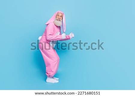 Full length photo of cheerful positive man pensioner dressed pink rabbit nightwear jumping empty space isolated blue color background