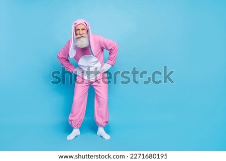 Full size photo of uncertain unsure elderly pensioner wear pink bunny costume hold hands on waist isolated on blue color background
