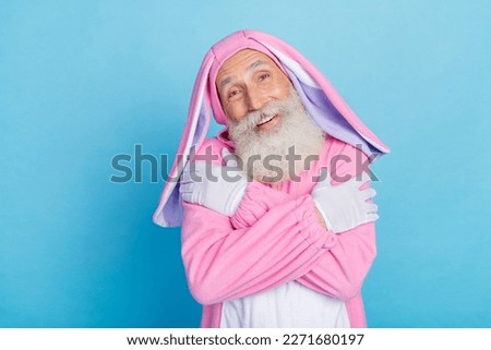 Photo of optimistic positive pensioner dressed pink bunny costume hug himself satisfied in comfort isolated on blue color background