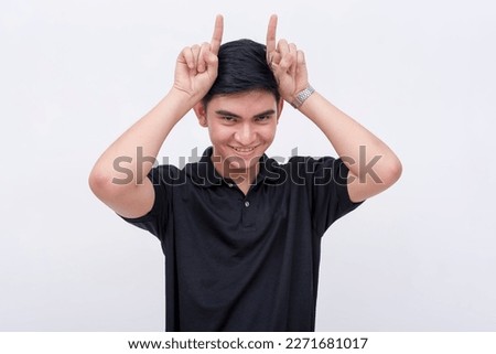 A devious man makes horns with two fingers like an devil, while looking at the camera. Isolated on a white backdrop.