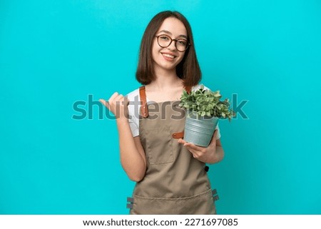 Gardener Ukrainian woman holding a plant isolated on blue background pointing to the side to present a product