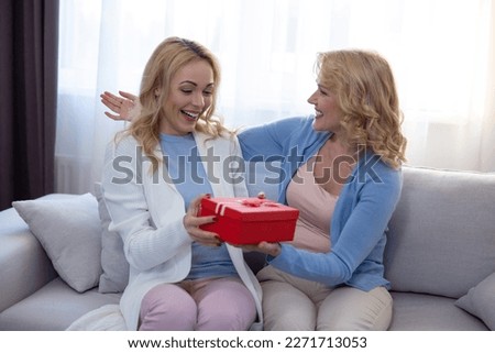 Joyous young blonde woman seated on the sofa accepting a gift from her loving mom