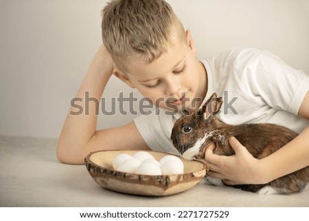 A little boy hugs the easter bunny rabbit, white eggs are near by, holiday concept