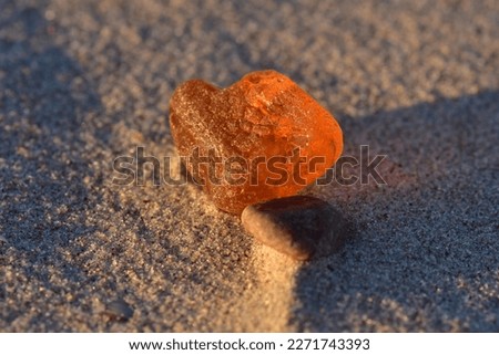 Transparent amber nugget and sea pebble on sand in the light of sunset. Nature gifts found on the Baltic sea shore beach. Macro. Selective focus. Royalty-Free Stock Photo #2271743393
