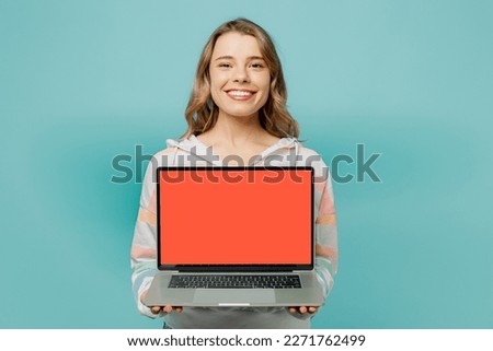 Young blonde IT woman wears striped hoody hold use work on laptop pc computer with blank screen workspace area isolated on plain pastel light blue cyan background studio portrait. Lifestyle concept