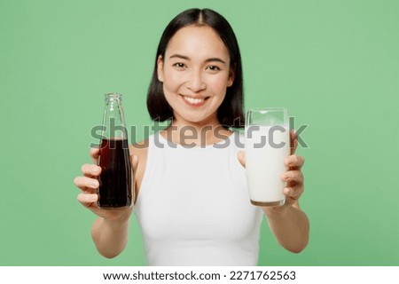 Young woman wearing white clothes hold in hands bottle of soda pop fizzy cola give glass of milk isolated on plain pastel green background. Proper nutrition healthy fast food unhealthy choice concept Royalty-Free Stock Photo #2271762563
