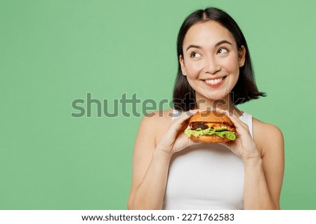 Young happy woman wear white clothes hold eat burger look aside on workspace area mockup isolated on plain pastel light green background. Proper nutrition healthy fast food unhealthy choice concept Royalty-Free Stock Photo #2271762583