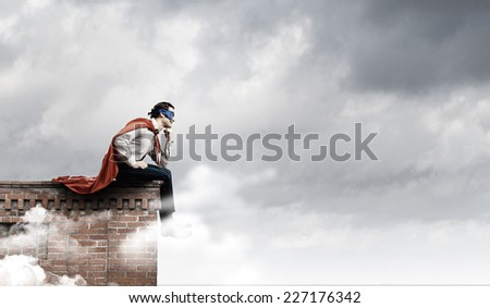 Young man in superhero costume sitting on top of building