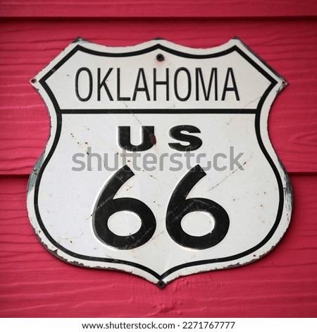Close-up on an Oklahoma US 66 route sign screwed on a wooden wall painted in red.