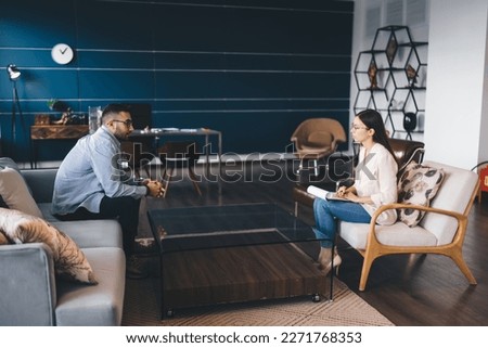 Side view of client having difficult situation sitting on sofa talking to psychotherapist during therapy consultation getting help from sessions Royalty-Free Stock Photo #2271768353
