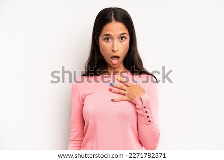 hispanic pretty woman feeling shocked, astonished and surprised, with hand on chest and open mouth, saying who, me?