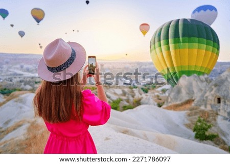 Girl traveling blogger takes photo on phone camera of flying hot air balloons in scenic valley in Nevsehir, Goreme. Beautiful destination in Anatolia, Kapadokya