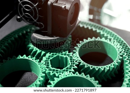 Detail view on print head of 3D-printer making a planetary gear part from mint coloured plastic. selective focus. Visible infill structure and layers at printed part. Modern production concept