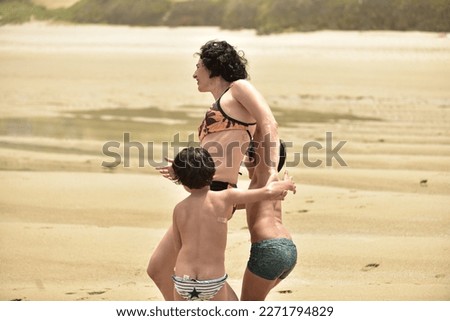 two children play fight with their mother on a beach