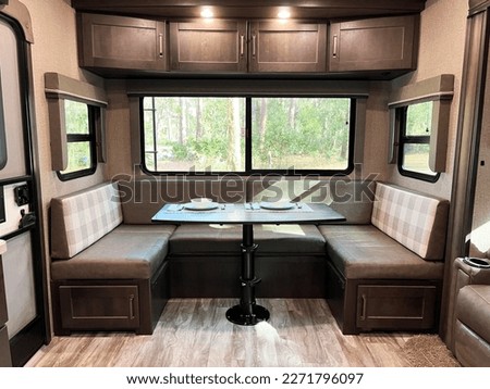 Modern, clean design of a fifth wheel travel trailer shows the dining area with storage and a huge picture window.