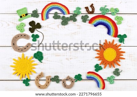 St Patrick's Day concept. Knitted composition of a green hat, a horseshoe, a sun, a rainbow and green shamrocks on a white wooden background. Copy space, flat lay