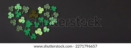 Composition made of knitted green shamrocks in the shape of a heart on a black background. Holiday sign and knitted clover leaf. Copy space, flat lay, banner. St Patrick's Day concept