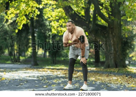 Sick man has severe heart pain after jogging, african american man holding hand to chest fast heart rate, tired sportsman on sunny day in park, using headphones and phone to listen to music. Royalty-Free Stock Photo #2271800071
