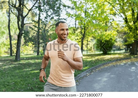 Cheerful and successful hispanic man jogging in the park, man running on a sunny day, smiling and happy having an outdoor activity. Royalty-Free Stock Photo #2271800077