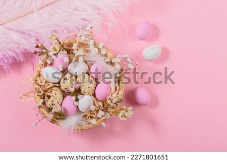 Easter candy chocolate eggs and almond sweets lying in a bird's nest decorated with flowers and feathers on pink background. Happy Easter concept.