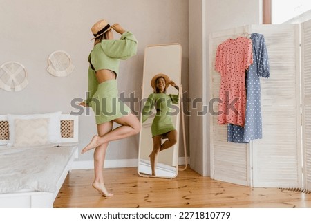 young pretty woman in green dress trying on fashion style trend dress looking in mirror at home or showroom Royalty-Free Stock Photo #2271810779