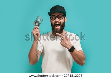 Fashionable bright man with a beard wearing white blank t shirt with copy space for your text or logo with an audio cassette in hand. Mockup for design