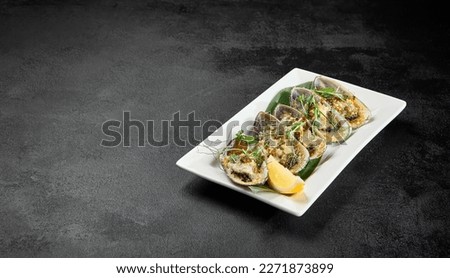 Baked mussels with cheese on plate on dark concrete background. Appetizer of mussels and lemon in minimal style on black table. Seafood menu. Prepared mussels on white plate