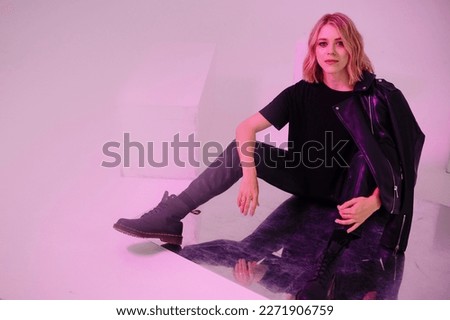 Beautiful young woman in wavy blond hair dressed in grunge style posing in studio with neon light. Confident fashion model indoors. Royalty-Free Stock Photo #2271906759