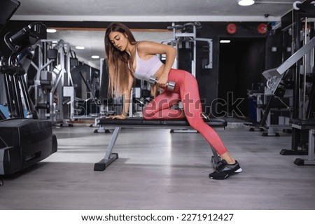 Exercise concept The female exercise doing dumbbell workout by resting her left knee and left hand on the bench and raise her right elbow up with a dumbbell in her hand.