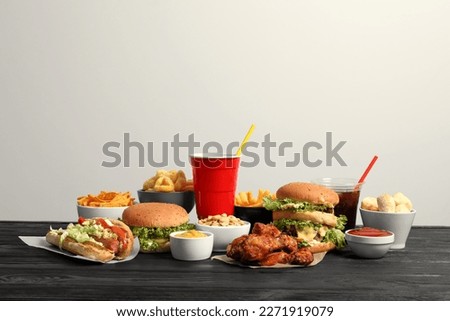 French fries, burgers and other fast food on wooden table against white background Royalty-Free Stock Photo #2271919079