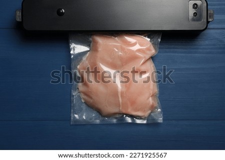 Sealer for vacuum packing and plastic bag with meat on blue wooden table, top view Royalty-Free Stock Photo #2271925567