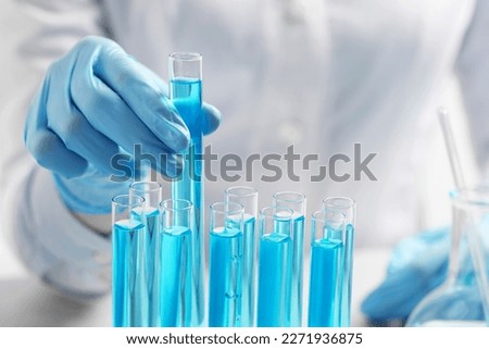 Scientist taking test tube with light blue liquid at table, closeup Royalty-Free Stock Photo #2271936875