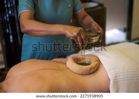 Woman having kati vasti Ayurveda treatment in spa while warm oil placing on her back Royalty-Free Stock Photo #2271938905