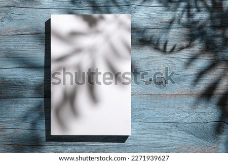 Canvas mockup, white blank picture hanging on blue wooden wall with dark shadows of palm leaves. Poster mock up, empty canvas with shadows of plant, front view