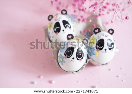 A composition with creatively colored Easter eggs with panda stickers and a branch on a pink background.