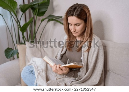 cozy bed and a beautiful girl, reading a book, concepts of home and comfort. Woman sitting on sofa with book in living room, enjoying her free time alone.