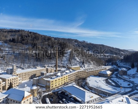 Aerial view from a drone of the old factory with a tall chimney on a sunny winter day in the town of Tanvald, Czech Republic