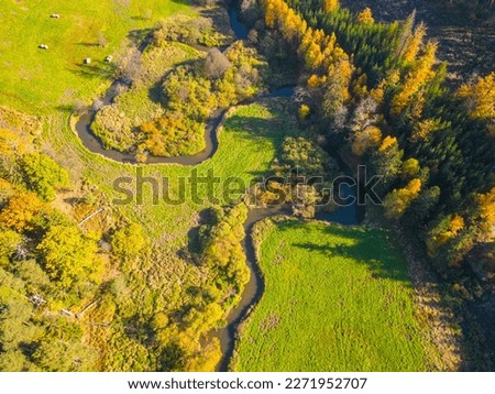 Narrow creek meanders in autumnal landscape. Green grass meadows and colourful trees. Aerial view from drone. Royalty-Free Stock Photo #2271952707