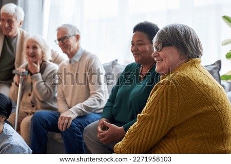 Side view at group of smiling senior people watching TV while sitting in row in retirement home facility