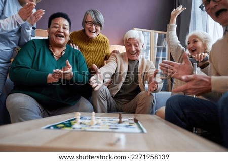 Multiethnic group of excited senior people playing board games at retirement home and celebrating win